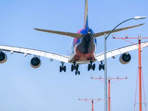 Un avion de ligne en approche d’atterrissage, train sorti, vu de l’arrière sous un ciel bleu.