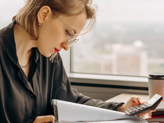 Une femme examine des documents financiers avec une calculatrice. Photographie d’illustration.